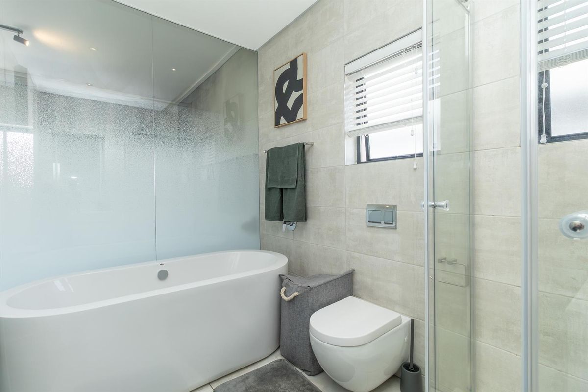 Modern bathroom featuring a sleek freestanding bathtub, a wall-mounted toilet, and a separate glass-enclosed shower with neutral wall tiling.