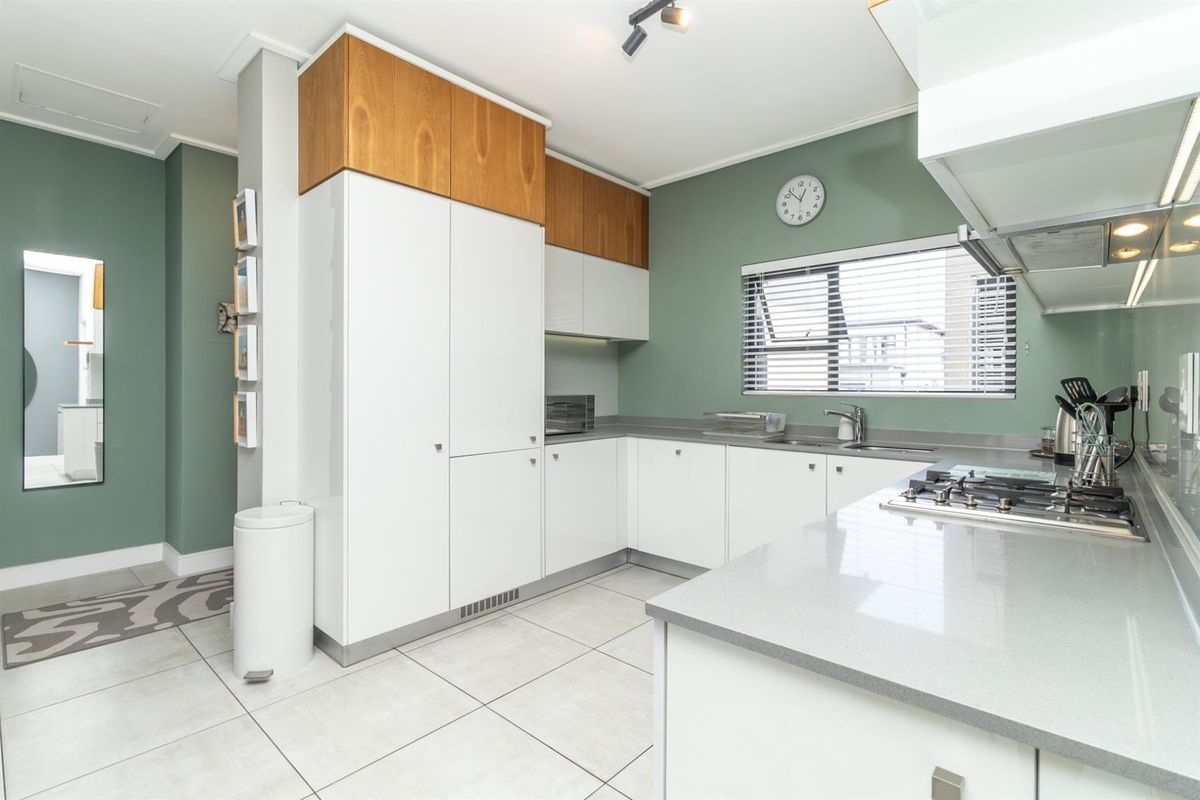 Modern kitchen featuring white and wood-tone cabinetry, stone countertops, gas hob, extractor fan, and tiled flooring with a clean, contemporary aesthetic.
