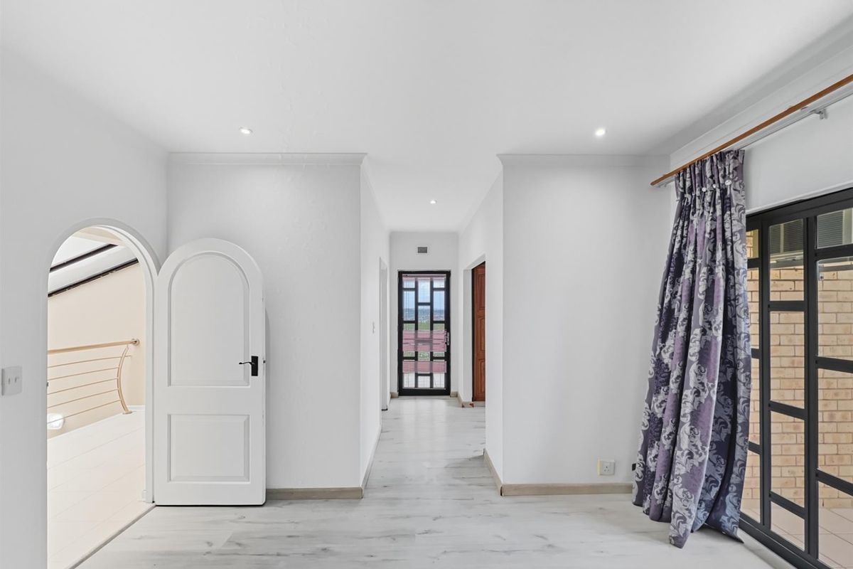 A bright, neutral interior space featuring light wood-look flooring, an arched doorway, and a glass-paneled exterior door leading to an outdoor area.