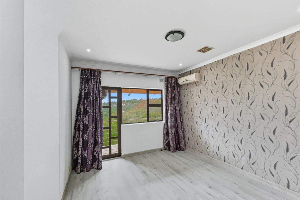 A bright bedroom featuring light wood-look flooring, a decorative feature wall, and direct access to an outdoor balcony area.