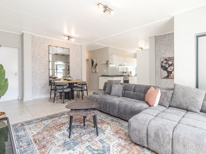 A bright open-plan living and dining area featuring tiled floors, modern kitchen cabinetry with built-in appliances, and neutral wall finishes.