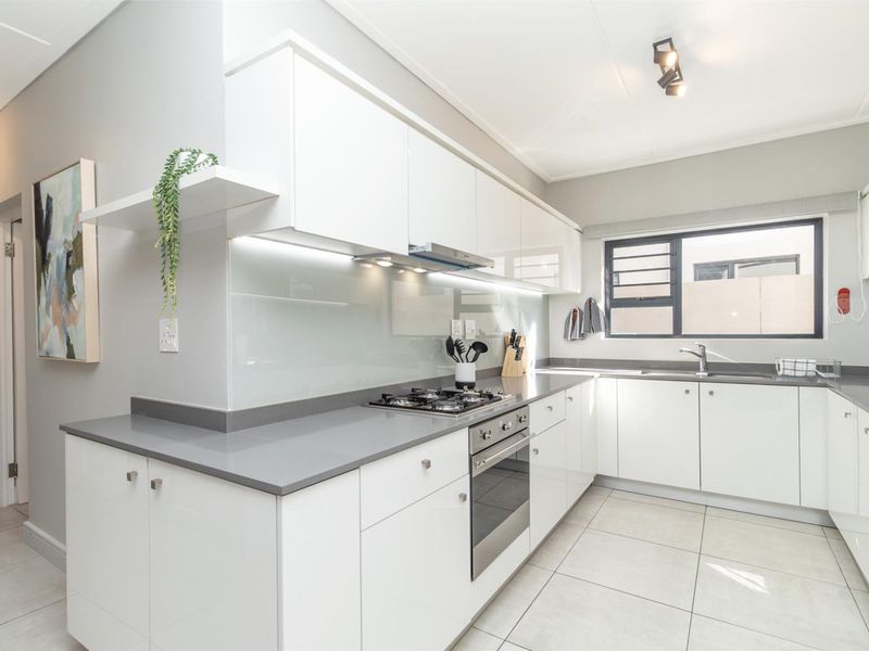 Modern kitchen featuring white high-gloss cabinetry, grey stone countertops, integrated gas hob, built-in oven, and sleek glass splashback with under-cabinet lighting.