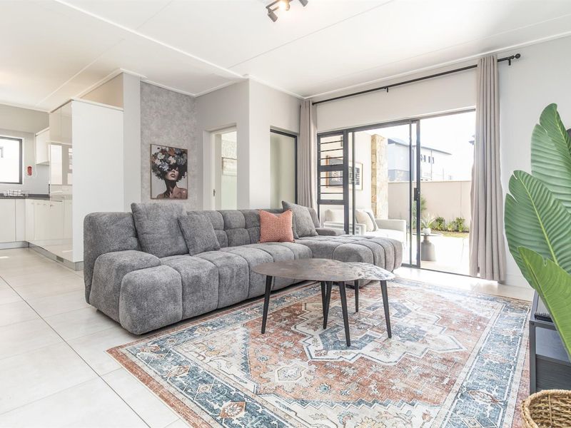 Bright open-plan living area featuring tiled floors and large sliding doors leading to an outdoor patio, seamlessly connected to a modern kitchen.