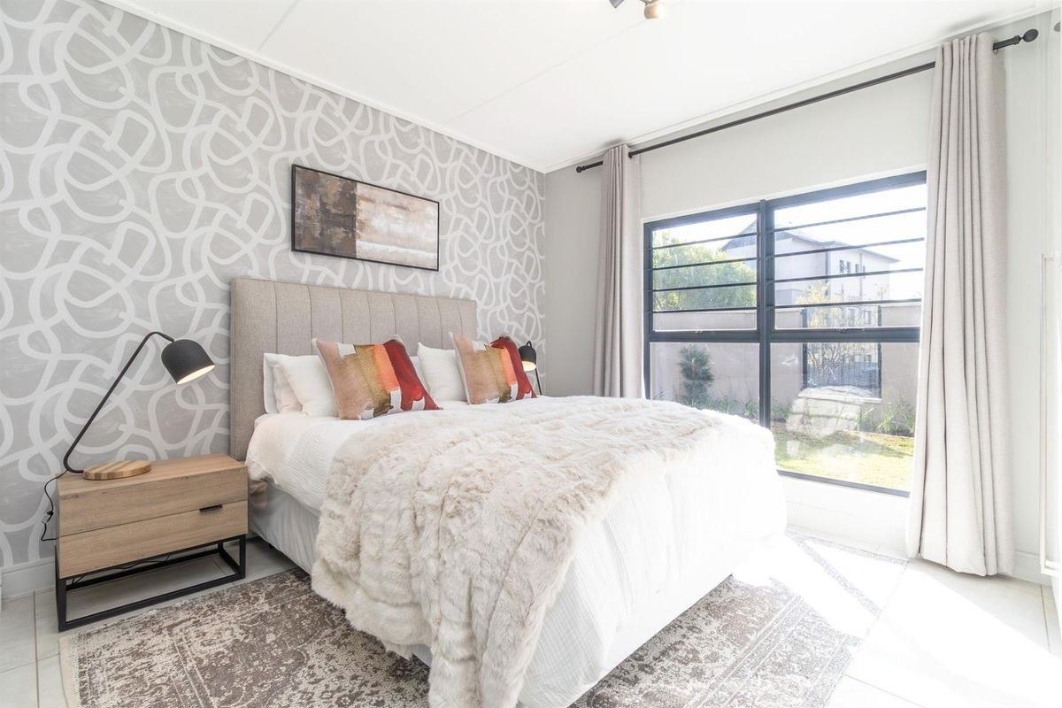 A well-lit bedroom featuring a large window with security bars and a decorative patterned accent wall.