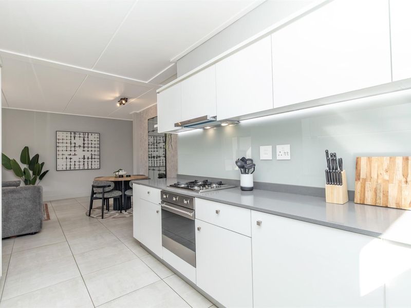 Modern open-plan kitchen featuring sleek white cabinetry, stone countertops, glass splashback, and integrated appliances, flowing seamlessly into the adjacent dining and living area.