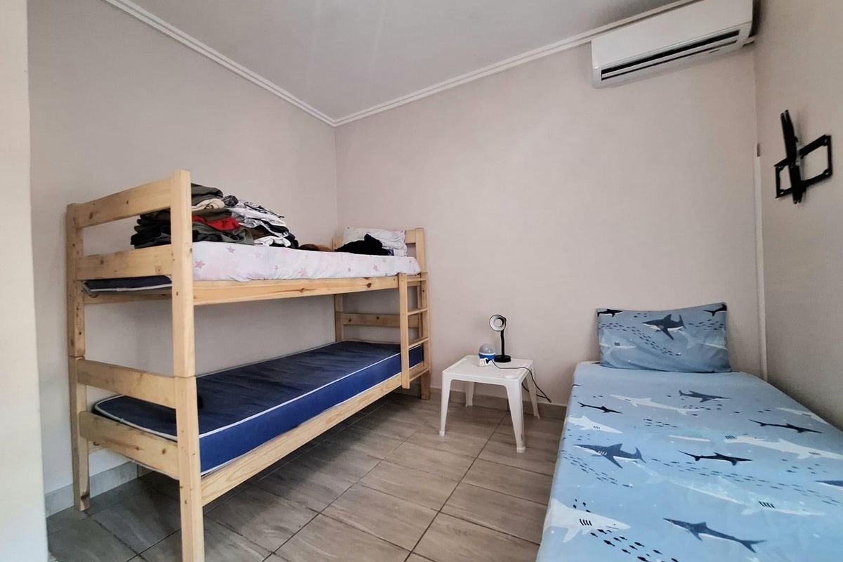 A functional bedroom featuring tiled flooring, a wall-mounted air conditioning unit, and a television wall mount.