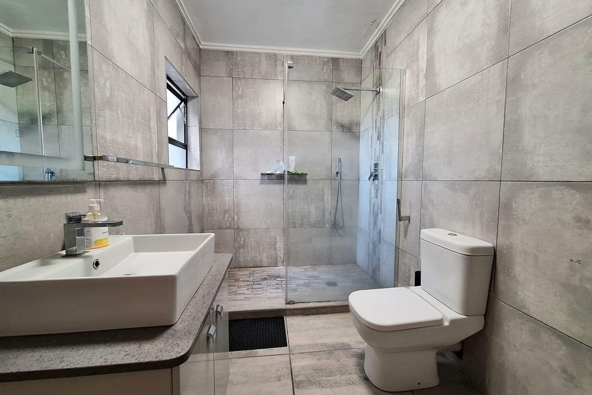 Modern bathroom featuring large-format grey wall tiles, a walk-in glass shower enclosure, a contemporary vanity with basin, and a white toilet.