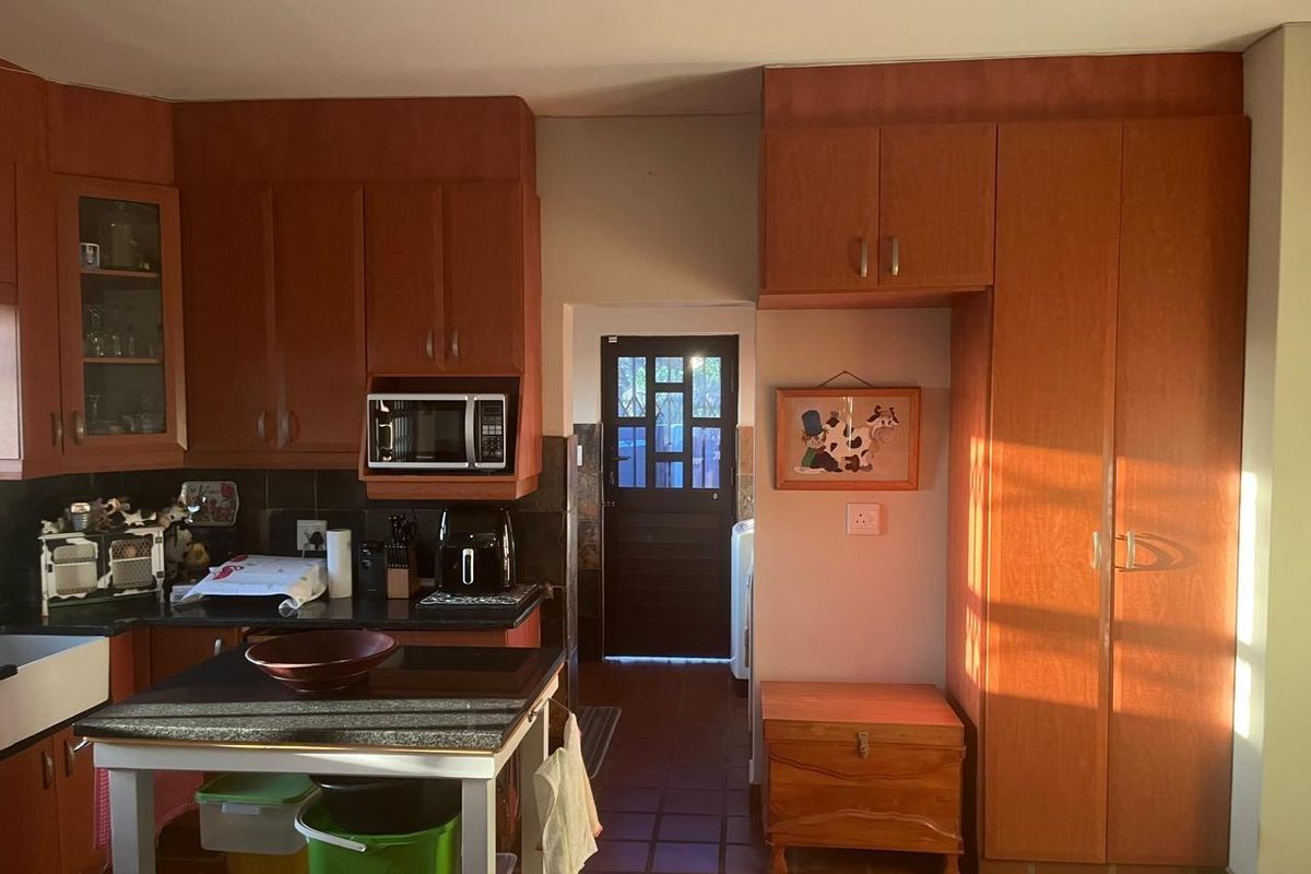 A functional kitchen featuring wood-toned cabinetry, dark granite countertops, and terracotta-style floor tiles, leading through to a rear utility access door.