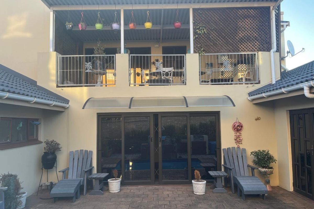 Rear view of the townhouse featuring a paved patio area, a covered upper-level balcony with metal railings, and sliding glass doors leading to the interior.