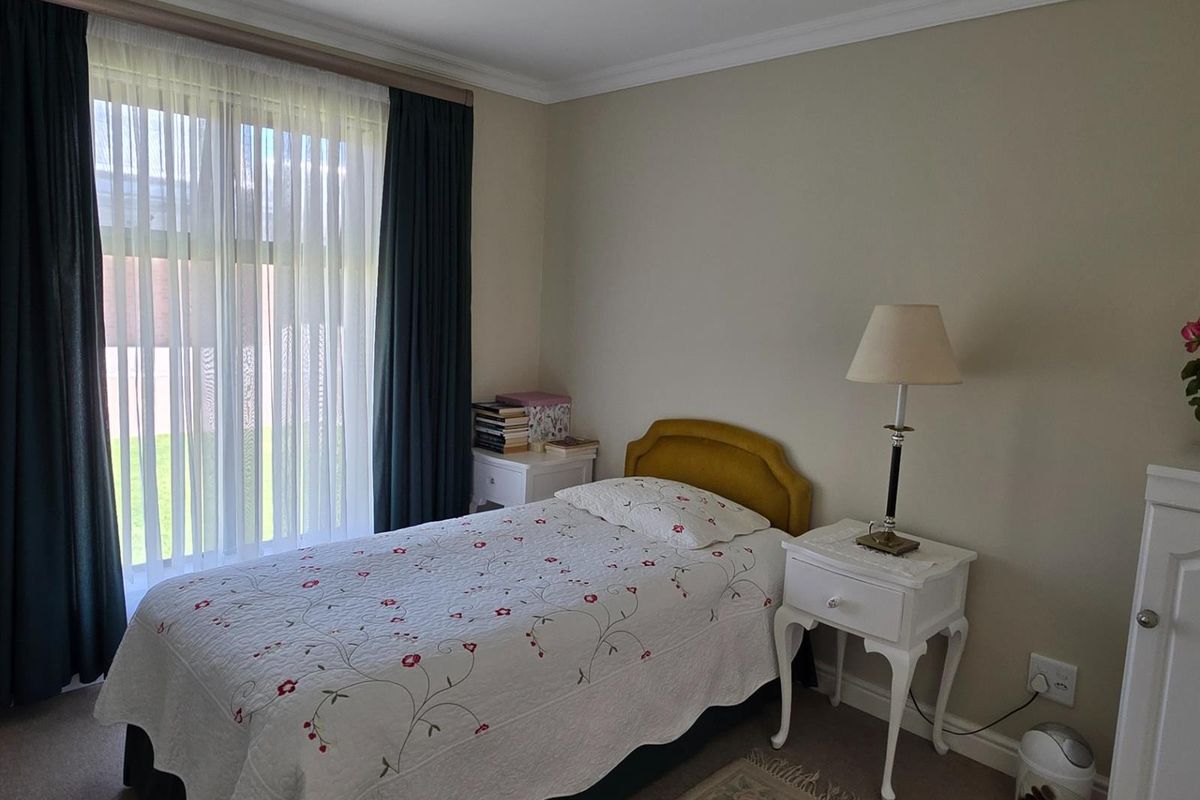 A well-maintained bedroom featuring neutral wall tones, carpeted flooring, and large windows with curtain tracks, providing a comfortable and functional living space.