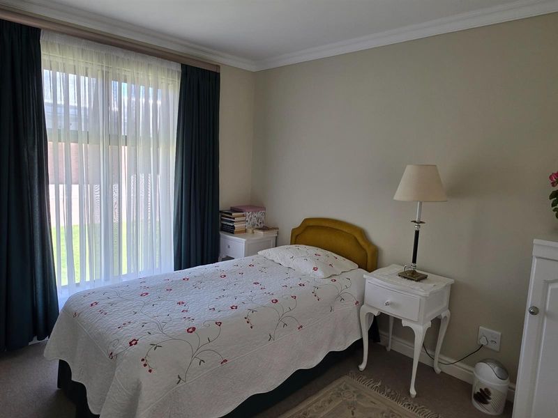 A well-maintained bedroom featuring neutral wall tones, carpeted flooring, and large windows with curtain tracks, providing a comfortable and functional living space.