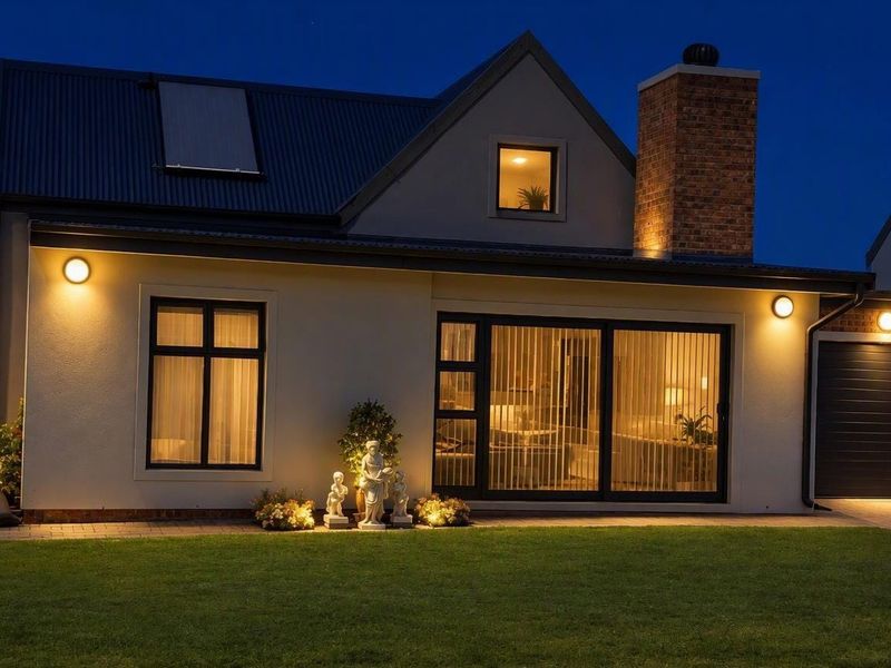 A well-maintained rear exterior view of a modern house at dusk, featuring a brick chimney, corrugated roof, and integrated outdoor lighting.