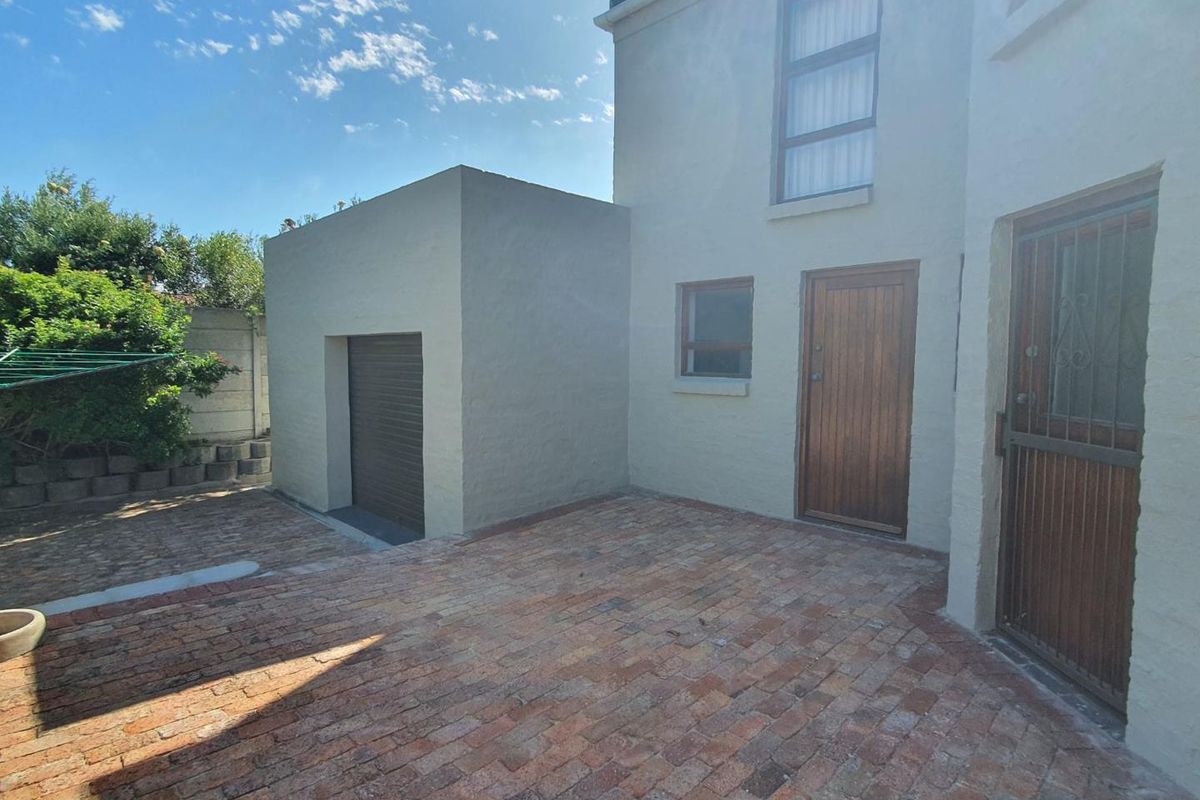 Rear exterior view of the house featuring a paved courtyard, a single garage, and access doors to the main dwelling.