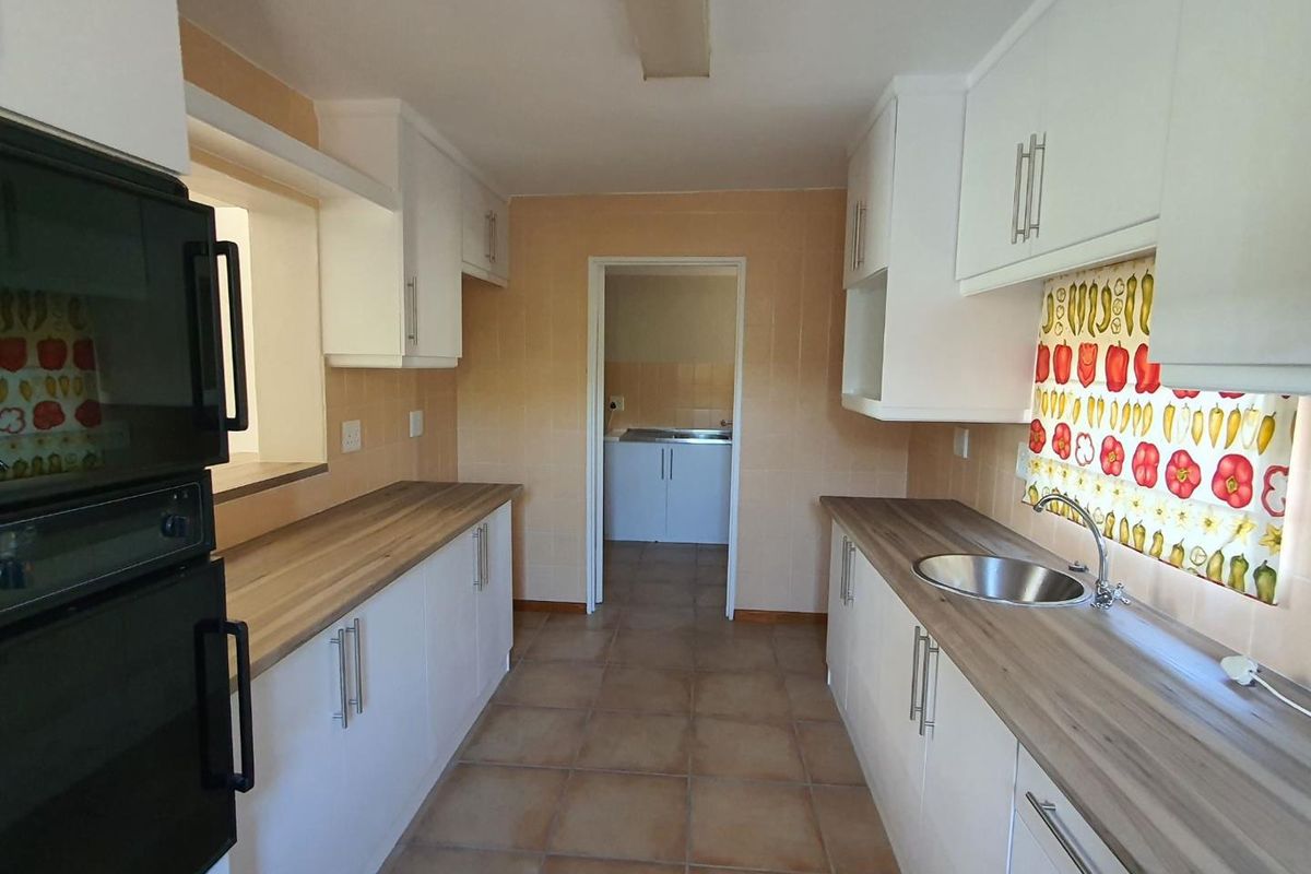 A functional galley-style kitchen featuring white cabinetry, wood-look countertops, a stainless steel sink, and a built-in oven, with an adjacent scullery area.