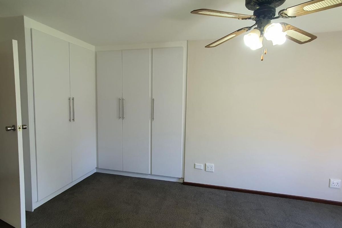 A clean bedroom featuring built-in white cabinetry, dark carpeting, and a ceiling fan with integrated lighting.