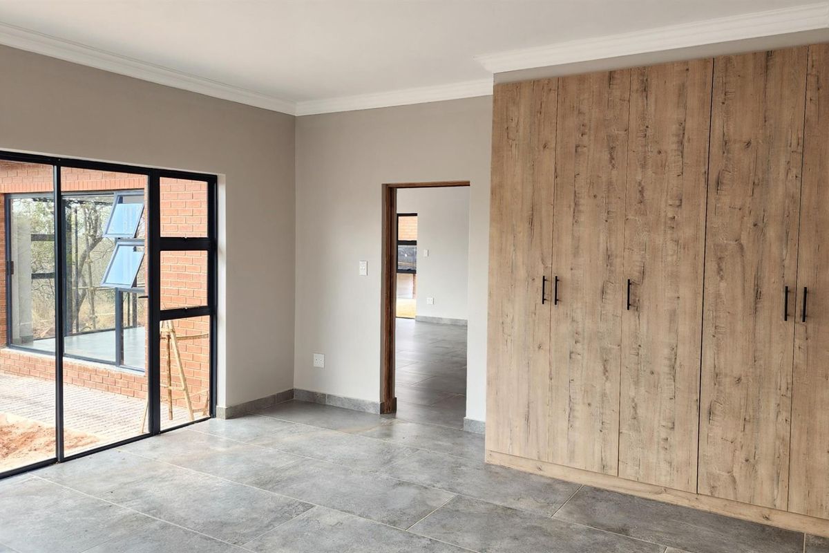 A modern bedroom featuring large sliding glass doors, tiled flooring, and extensive built-in wooden cabinetry with contemporary black hardware.