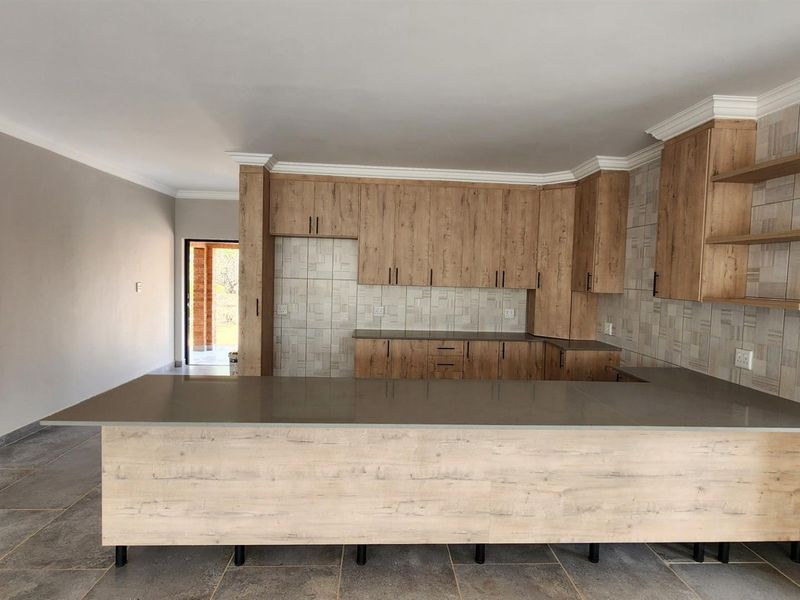 Modern open-plan kitchen featuring wood-grain cabinetry, stone countertops, a breakfast bar, and tiled backsplash, seamlessly integrated into the living area.