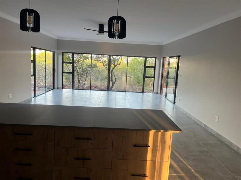 Spacious open-plan living area featuring large floor-to-ceiling windows, modern tiled flooring, and a central kitchen island with wood-finish cabinetry.