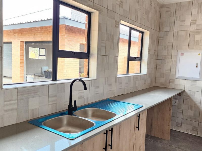 A modern kitchen featuring light wood-grain cabinetry, stone-look countertops, a double stainless steel sink with a matte black faucet, and tiled wall finishes.