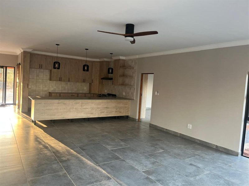Spacious open-plan kitchen and living area featuring modern wood-look cabinetry, a breakfast bar, tiled flooring, and a ceiling fan.
