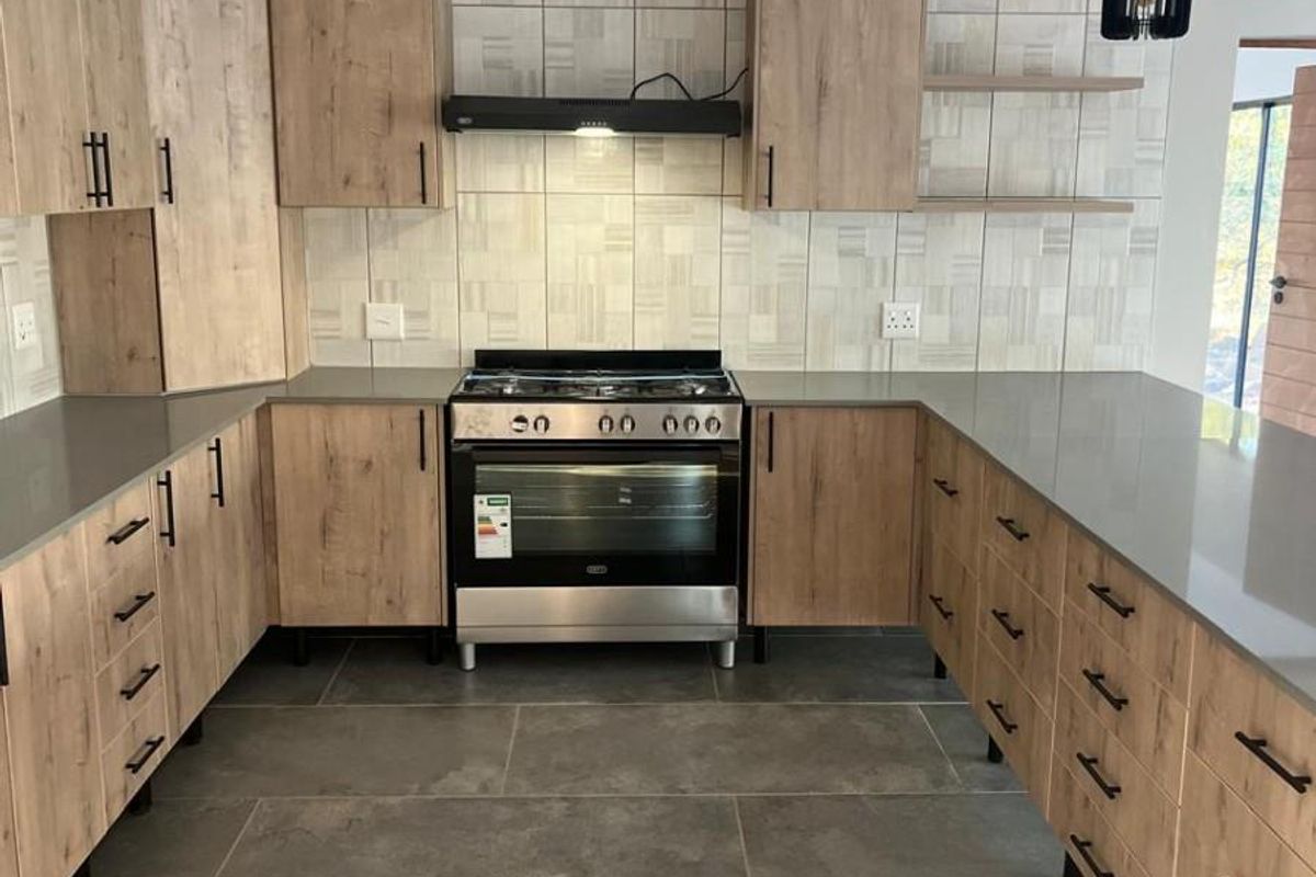 Modern U-shaped kitchen featuring wood-grain cabinetry, stone-look countertops, tiled backsplash, and a built-in gas stove with extractor fan.