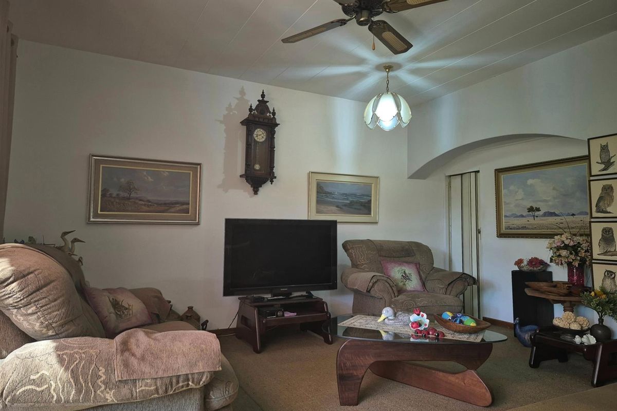 A comfortable living room featuring a ceiling fan, arched architectural detail, and carpeted flooring.