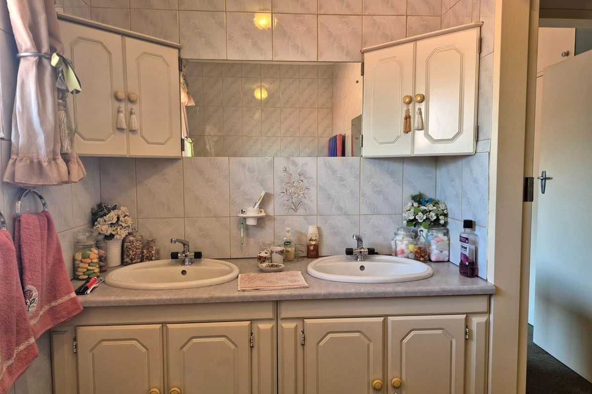 A functional bathroom vanity area featuring dual drop-in sinks, laminate countertop, and ample overhead storage cabinetry with integrated wall-mounted mirror.