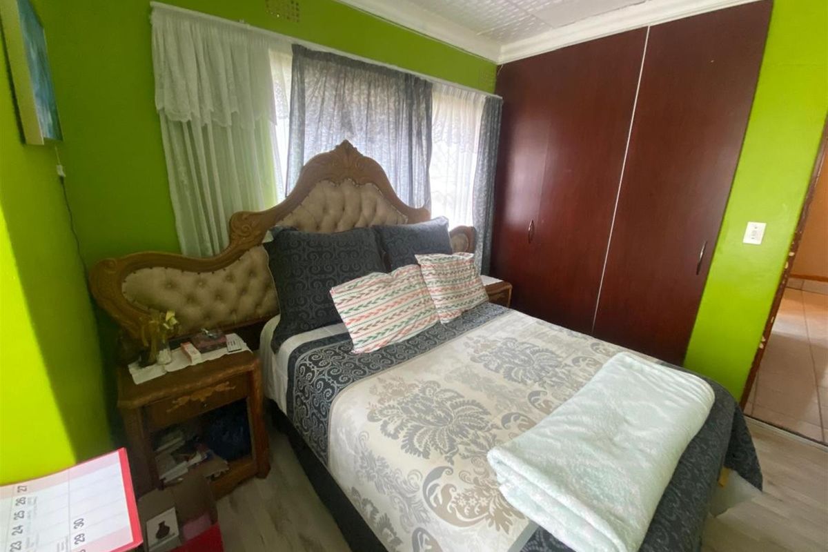 A bedroom featuring built-in wooden cupboards, light-toned flooring, and a large window with curtain treatments.