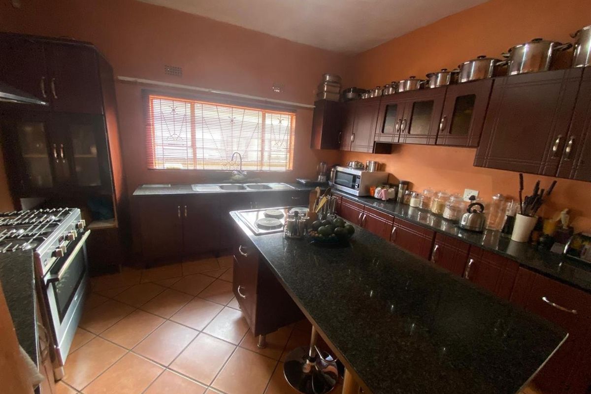 A functional kitchen featuring dark wood cabinetry, granite countertops, a central island, and tiled flooring.