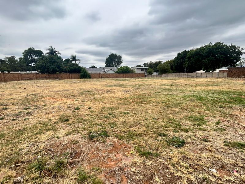 A vacant commercial land plot featuring perimeter brick boundary walls and open grassed terrain, suitable for future development.