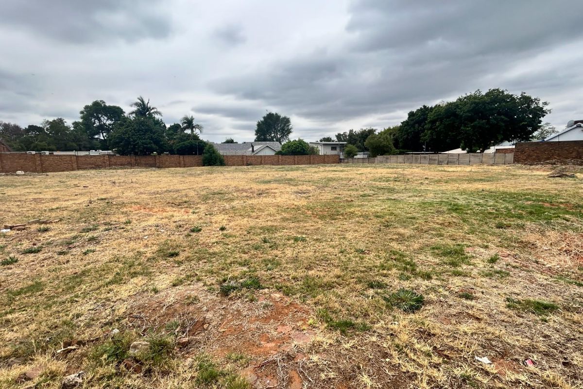 A vacant commercial land plot featuring perimeter brick boundary walls and open grassed terrain, suitable for future development.