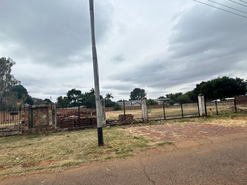 A vacant commercial land plot featuring perimeter metal fencing, brick pillars, and street-level access, suitable for future development.