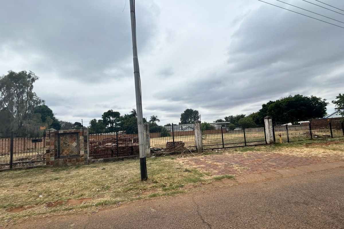 A vacant commercial land plot featuring perimeter metal fencing, brick pillars, and street-level access, suitable for future development.