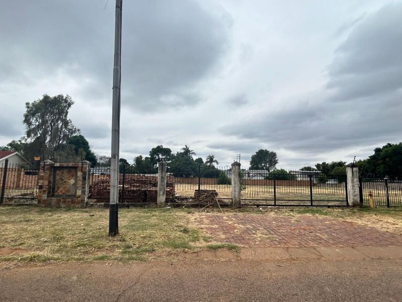 A vacant commercial plot featuring perimeter fencing, brick pillars, and a paved entrance area, offering a clear site for future development.
