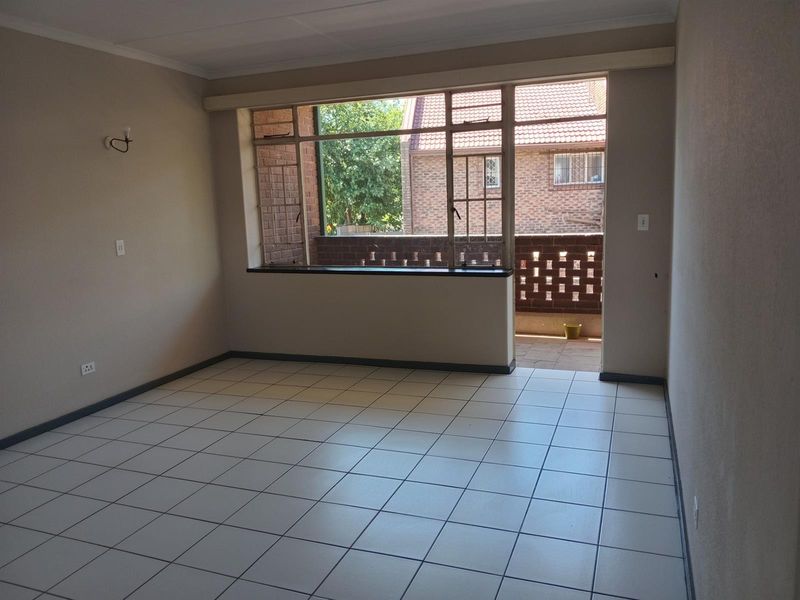An empty, well-lit living room featuring neutral tiled flooring and direct access to an outdoor balcony area.