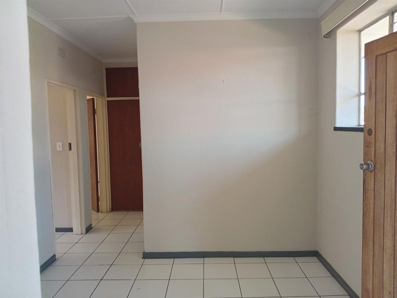 A clean, empty hallway featuring neutral tiled flooring, built-in storage cupboards, and internal wooden doors.