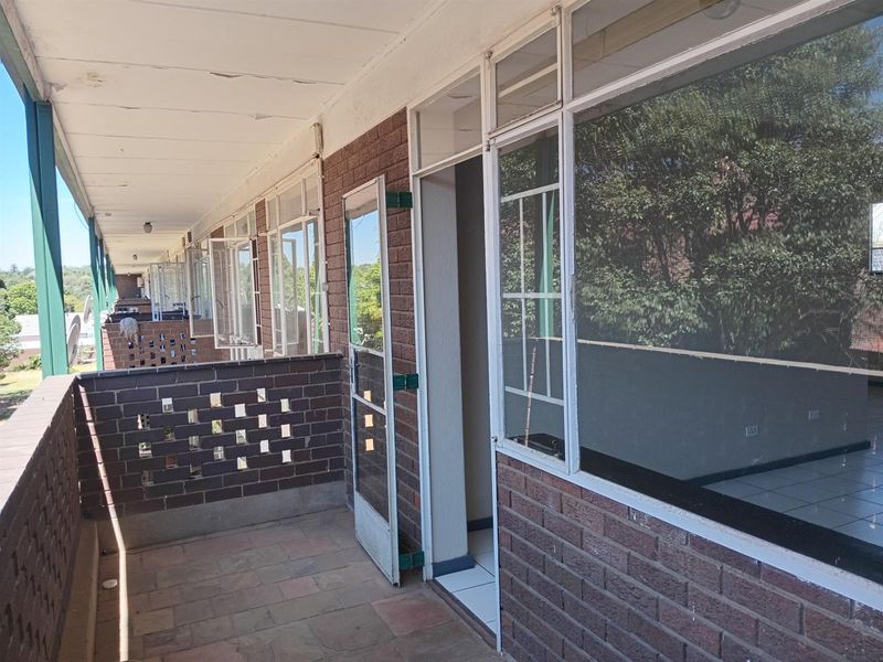 A covered balcony area featuring brick walls, tiled flooring, and large windows providing access to the apartment interior.