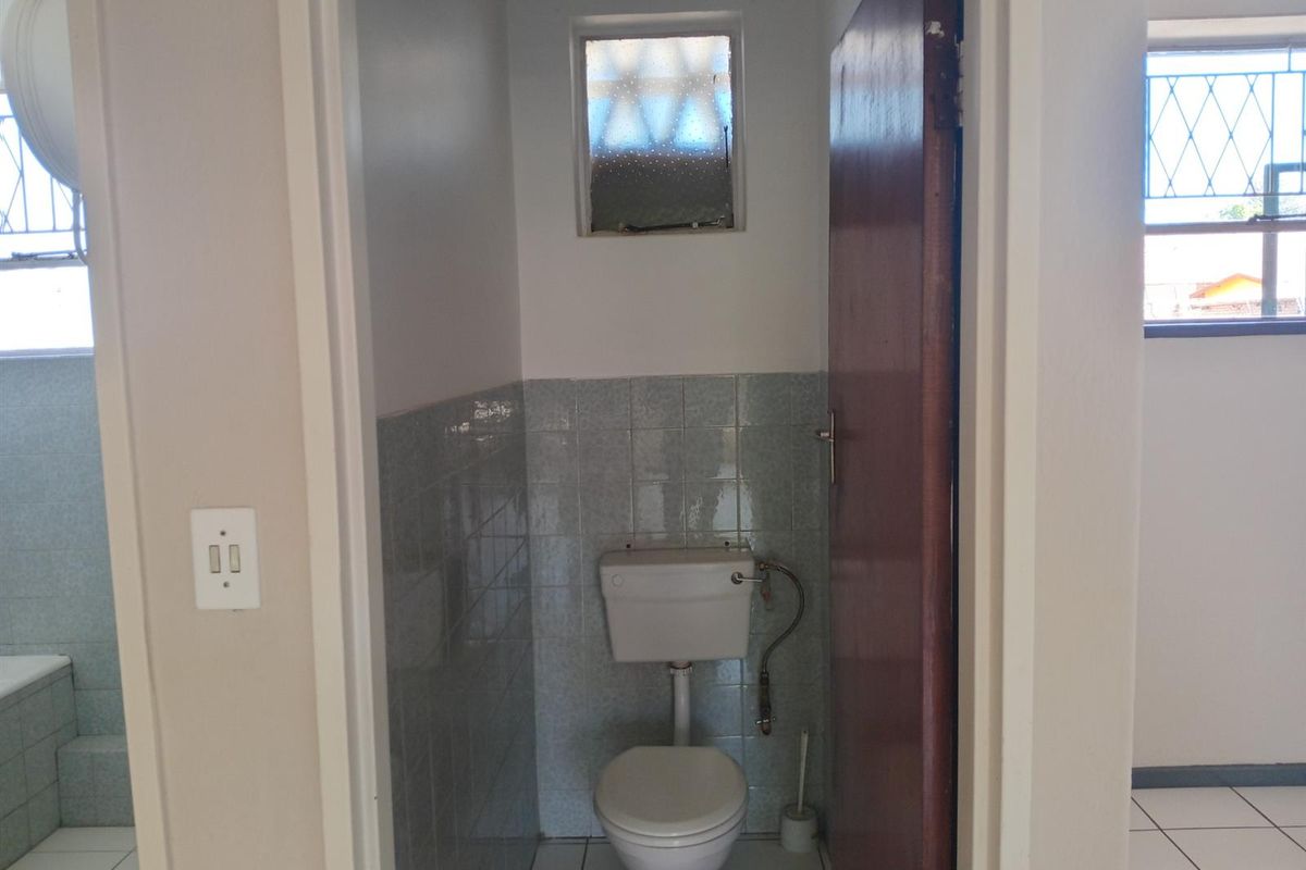 A compact, dated bathroom featuring ceramic wall and floor tiles, a standard toilet, and an obscured glass window for privacy.