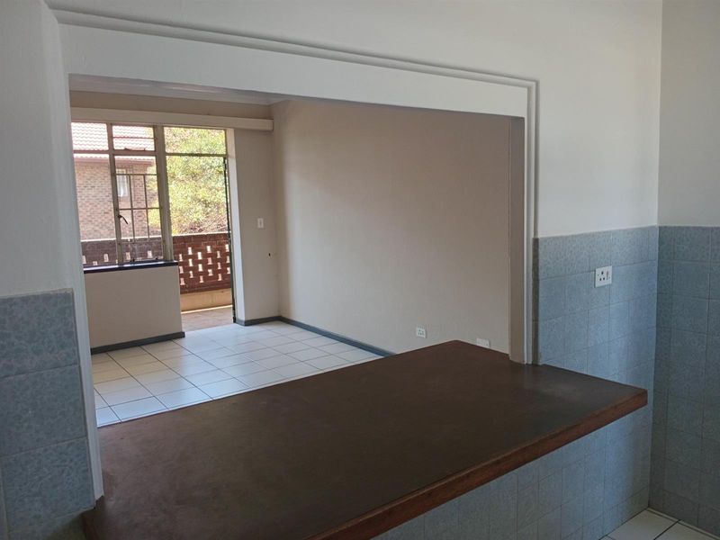 Open plan kitchen area featuring a breakfast bar, tiled splashbacks, and direct access to a balcony, offering a functional and versatile living space.