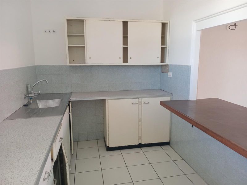 A dated, empty kitchen featuring laminate countertops, built-in cabinetry, a stainless steel sink, and a breakfast bar, ready for renovation.