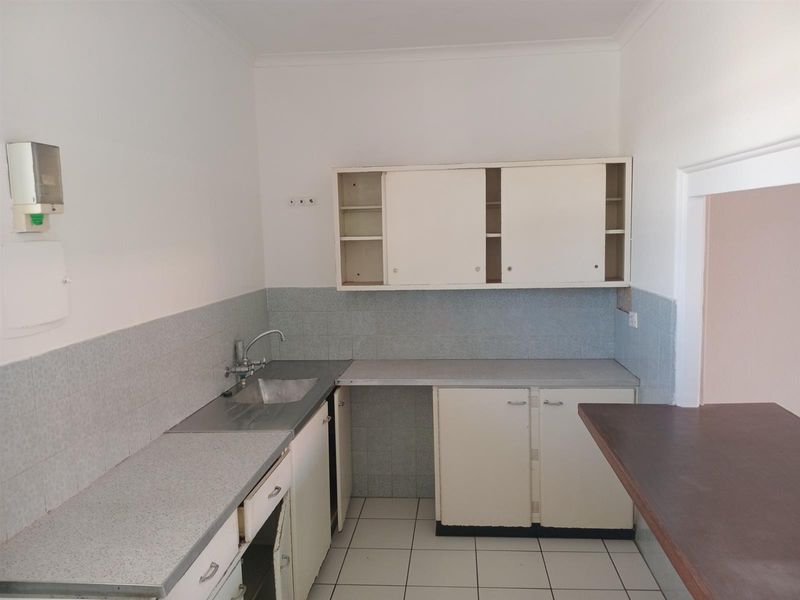 A dated kitchen featuring built-in cabinetry, laminate countertops, a stainless steel sink, and a breakfast bar, ready for renovation and modernization.