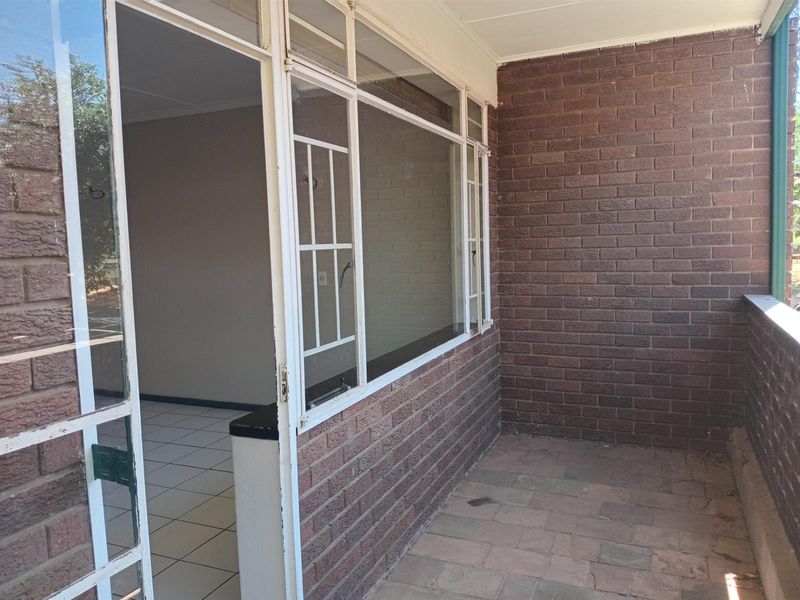 A covered balcony area featuring exposed brick walls and tiled flooring, providing a functional outdoor space with direct access to the interior.