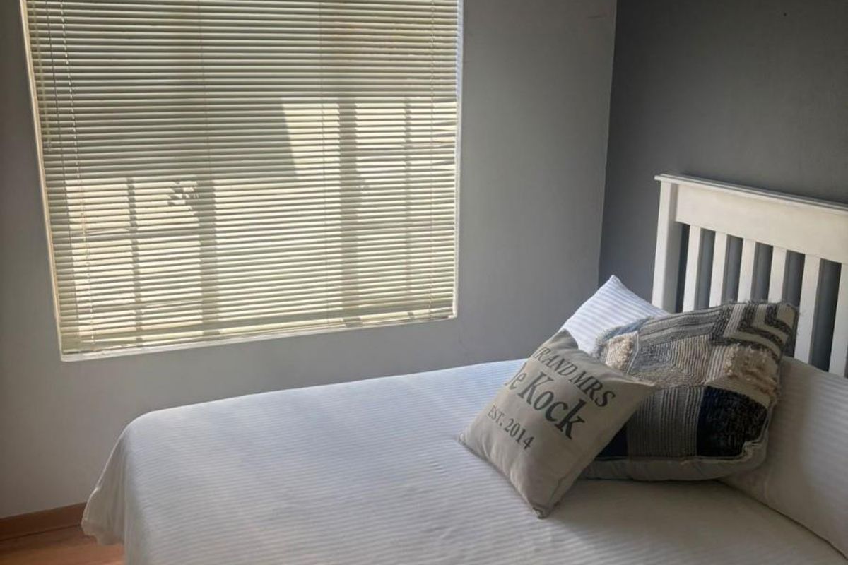 A bedroom featuring laminate flooring, a window with fitted blinds, and a dark accent wall.