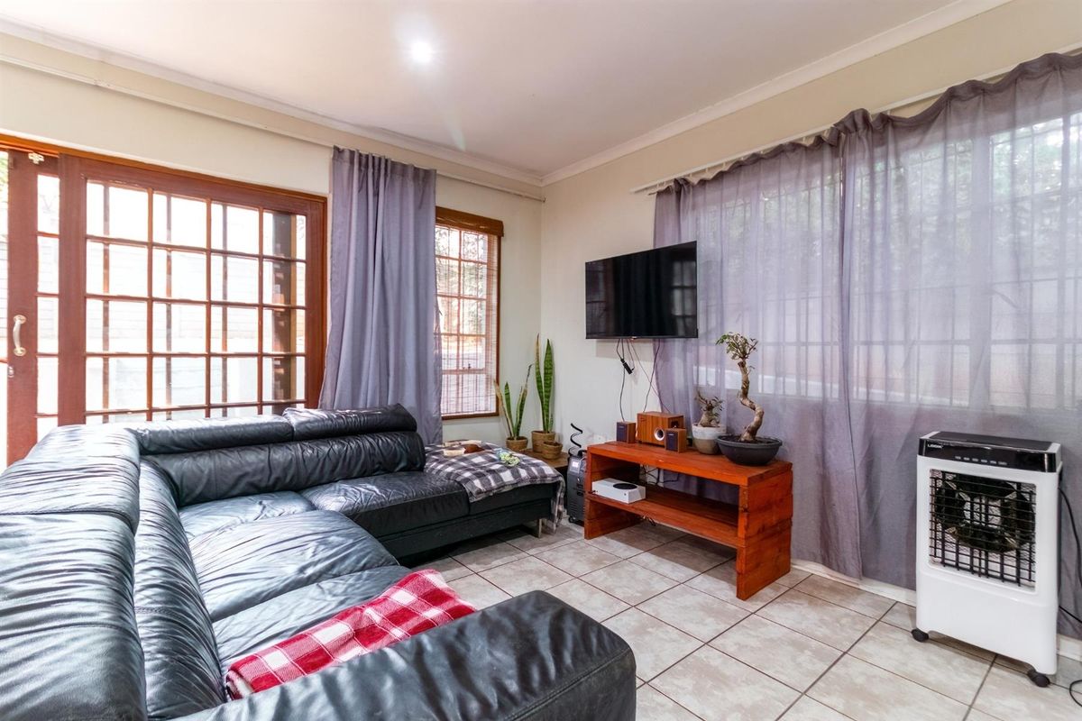 A living room featuring tiled flooring, large wooden-framed glass doors, and windows with curtain tracks.
