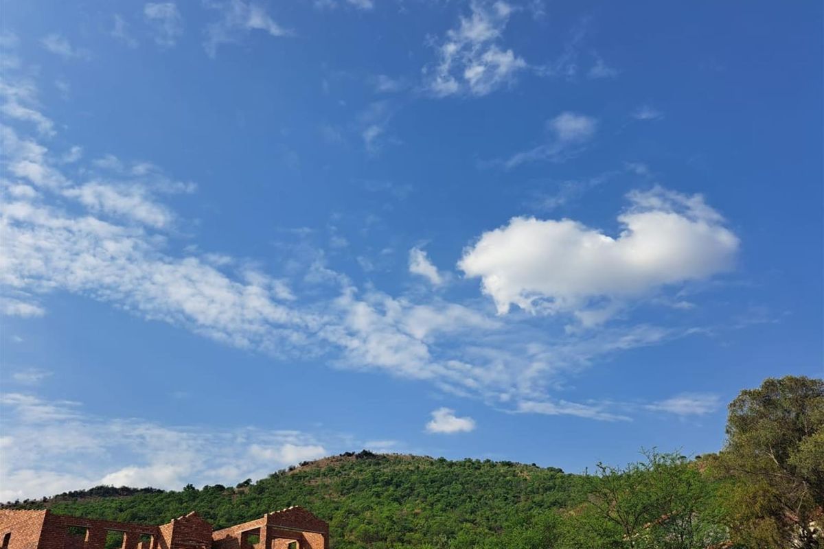 A view of an unfinished brick residential structure set against a scenic mountain landscape and clear blue sky.