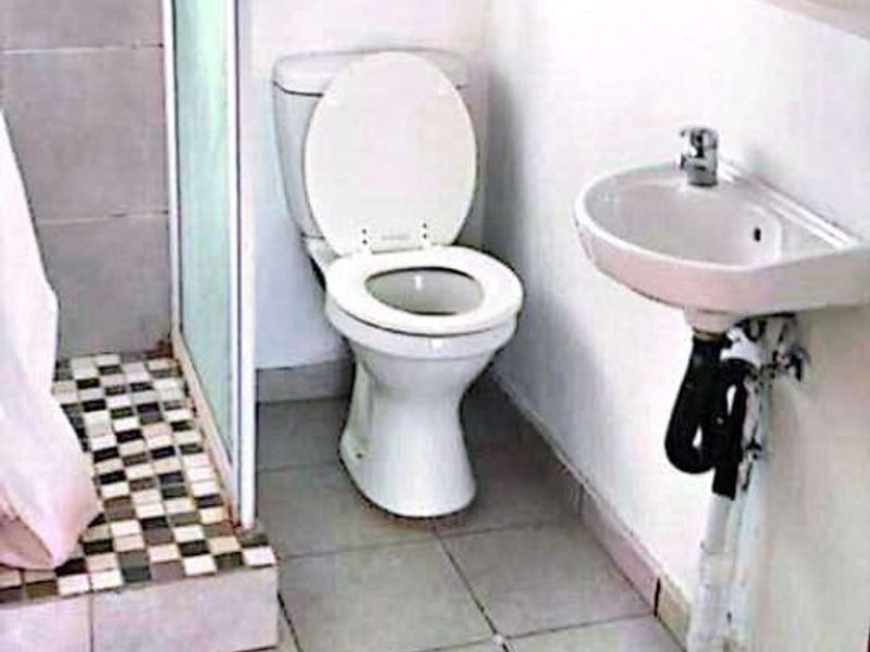 A functional bathroom featuring a shower enclosure, toilet, and wall-mounted basin with tiled flooring throughout.