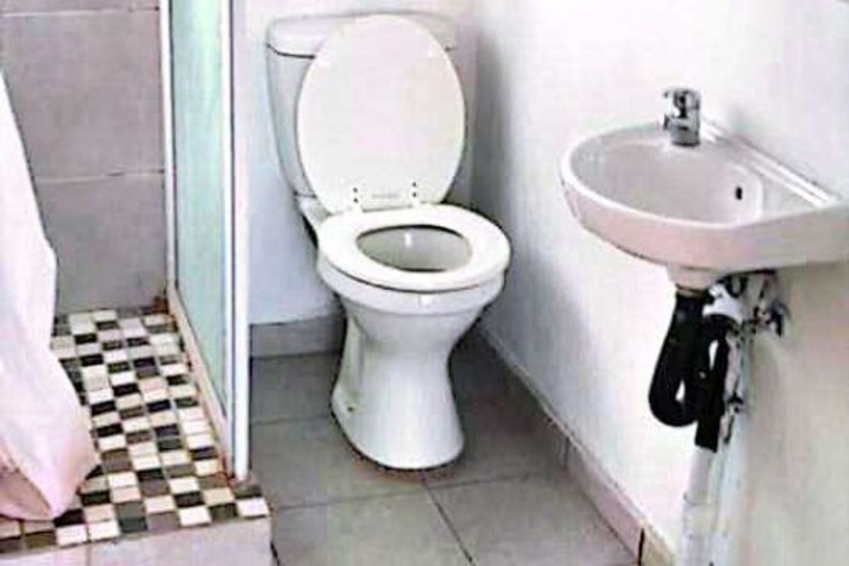 A functional bathroom featuring a shower enclosure, toilet, and wall-mounted basin with tiled flooring throughout.