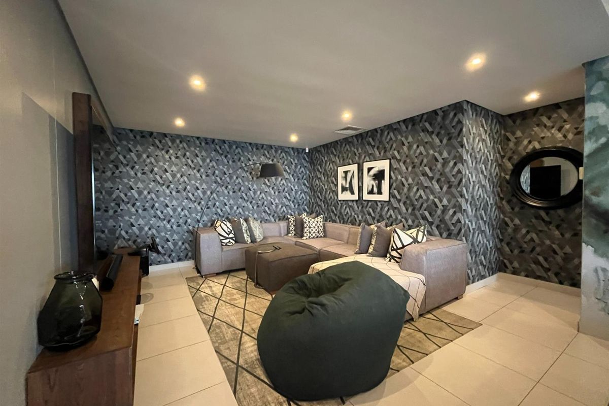 A modern living room featuring geometric patterned wallpaper, recessed downlighting, and large format floor tiles.