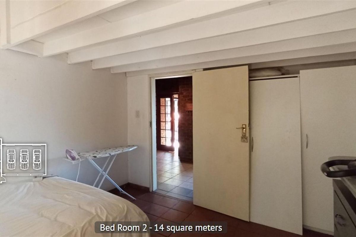 A bedroom featuring exposed white ceiling beams, built-in wardrobe storage, and tiled flooring, with direct access to an adjacent living area.