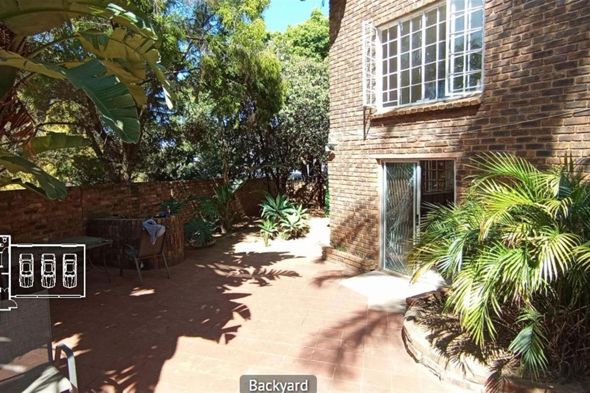 A private rear courtyard featuring brick paving, established garden beds, and direct access to the home through sliding glass doors.